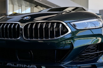 A close-up view of a luxury car's front grille and headlight. The image features sleek, reflective surfaces with intricate design elements, showcasing a modern and sophisticated style.