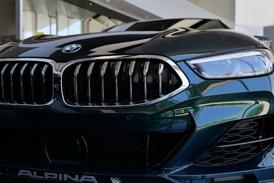 A close-up view of a luxury car's front grille and headlight. The image features sleek, reflective surfaces with intricate design elements, showcasing a modern and sophisticated style.