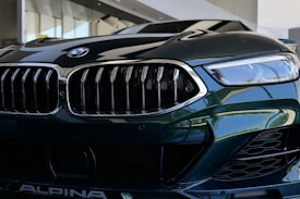 A close-up view of a luxury car's front grille and headlight. The image features sleek, reflective surfaces with intricate design elements, showcasing a modern and sophisticated style.