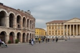 a group of people walking around a courtyard with buildings in the background with Verona in the background