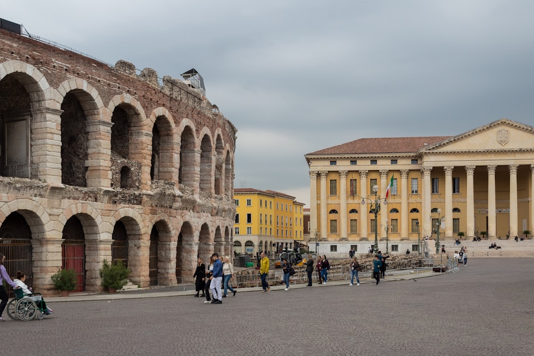 a group of people walking around a courtyard with buildings in the background with Verona in the background, Arena di Ve