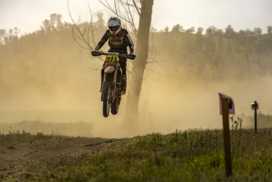 Dynamic motocross rider racing through rugged terrain at sunset with dust flying.