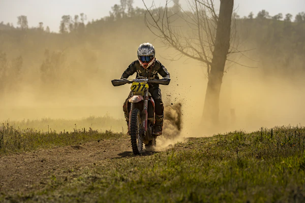 Dynamic shot of a rider wearing full protection gear speeding through a dusty trail.