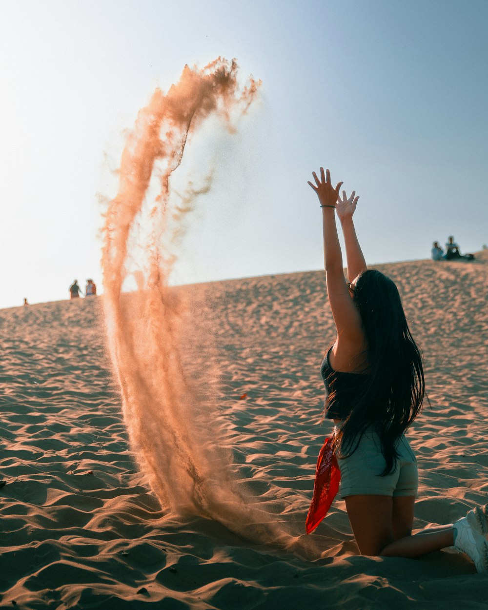 a woman sitting on the beach with her hands up in the air