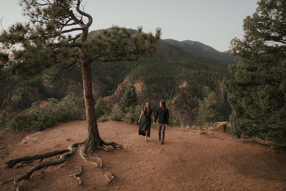 a man and woman walking on a dirt path in the mountains