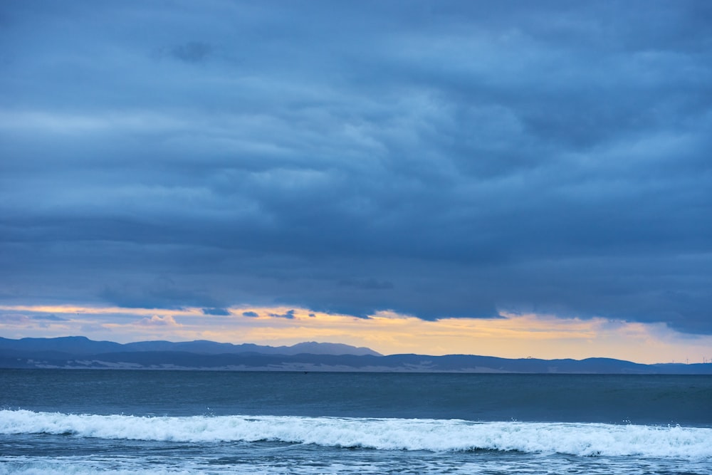 a body of water with waves and mountains in the background