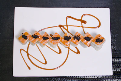 Close-up of a vibrant salmon dragon roll artfully plated on a sleek black dish with gold accents.