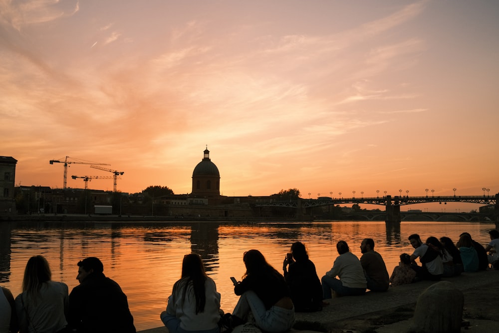 a group of people sitting on a dock looking at a building