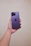 A happy young woman holding a new smartphone with a bright lilac background.