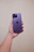 A happy young woman holding a new smartphone with a bright lilac background.