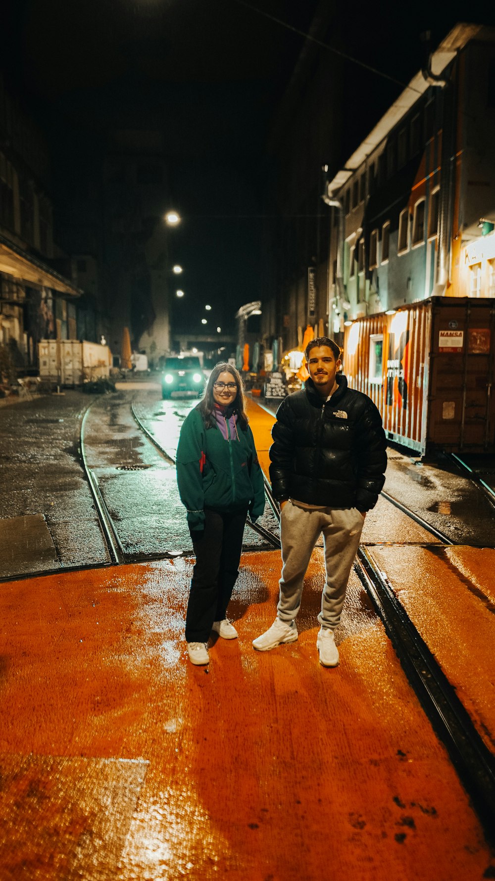 a man and woman standing on a wet street at night