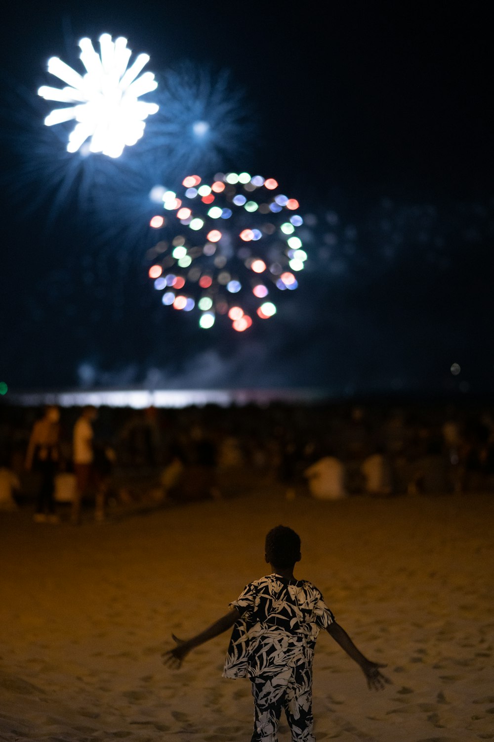 uma criança correndo em uma praia com fogos de artifício no céu