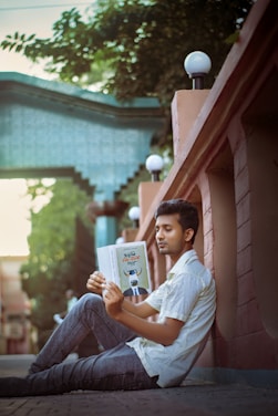 a person sitting on a ledge reading a book