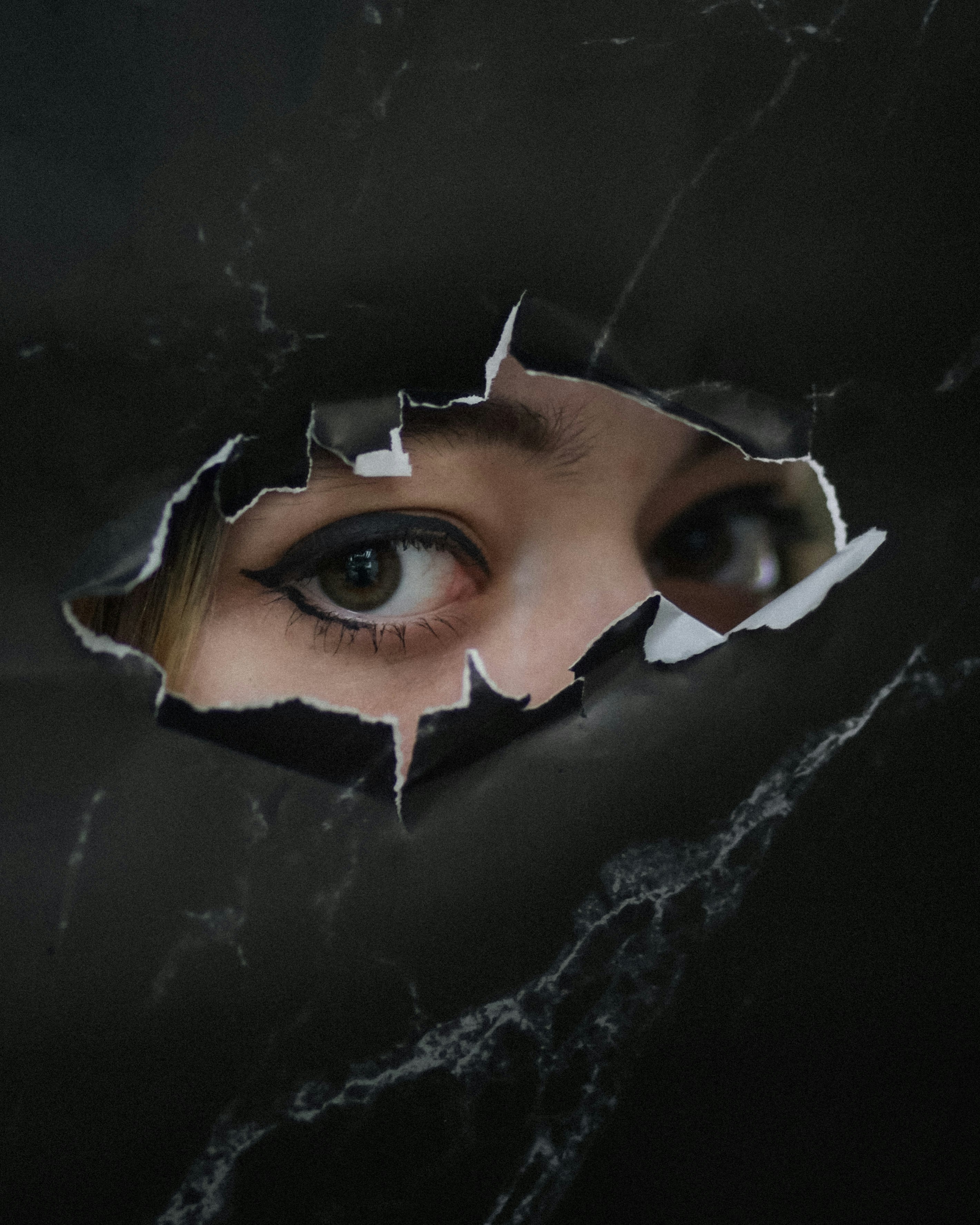 Woman's eyes peeking through a torn black surface