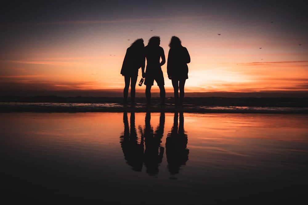 a group of people standing on a beach at sunset