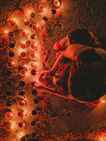 A serene morning scene with a person lighting a diya (oil lamp) beside a small altar adorned with flowers and sacred idols.