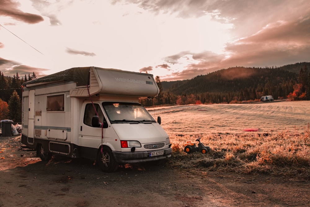 a white van parked on a dirt road with a hill and trees in the background