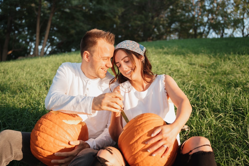 a man and woman sitting on a pumpkin in a grassy field