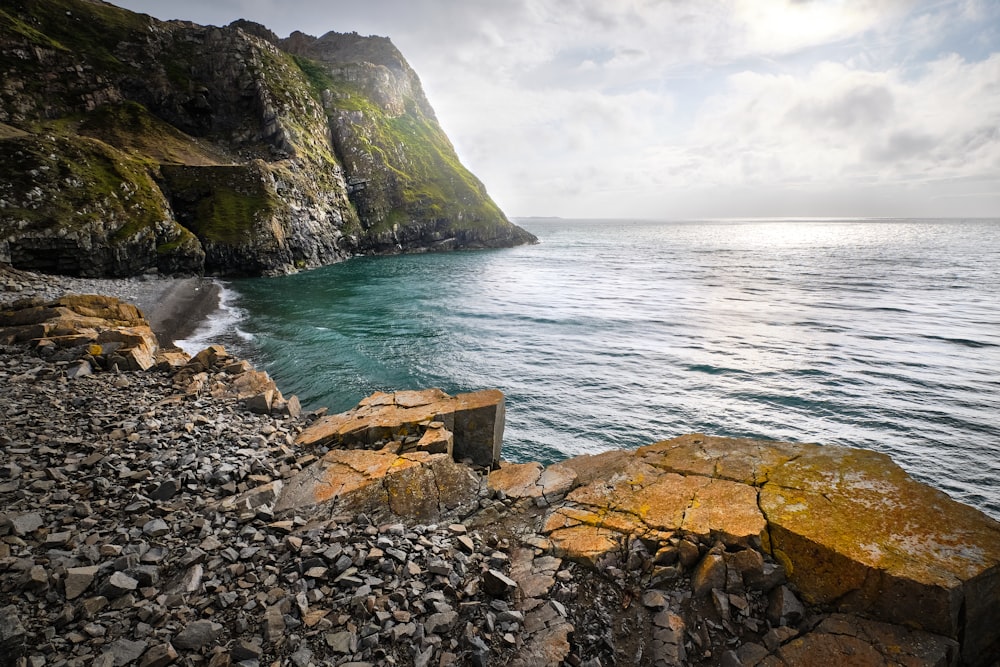 a rocky beach with a body of water and a hill with a hill