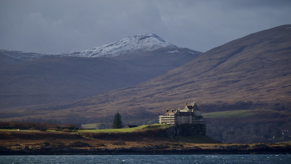 a building on a hill by a body of water with a mountain in the background