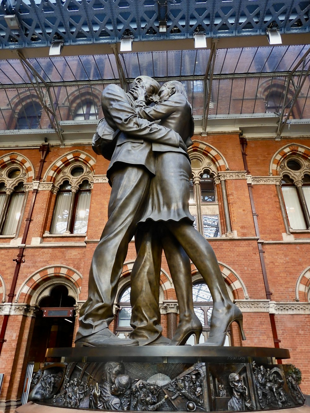 eine Statue eines Mannes und einer Frau mit dem Bahnhof St. Pancras im Hintergrund