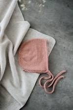 Close-up of a delicate handmade crochet baby cap with soft pastel colors, lying on a wooden table.