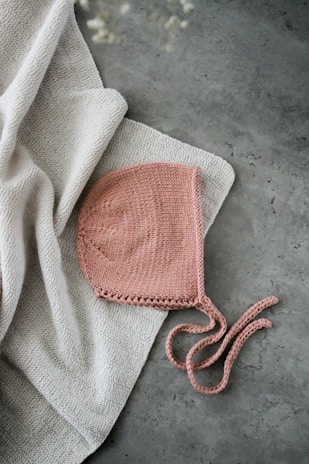 Close-up of a delicate handmade crochet baby cap with soft pastel colors, lying on a wooden table.