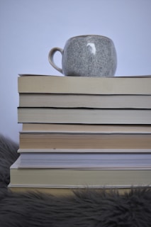 An overhead shot of a single mug beside a small stack of books and a cozy knitted blanket