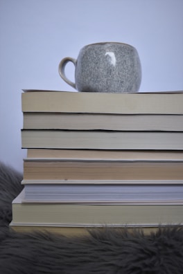 A serene stack of books with a delicate terracotta ceramic cup resting on top, set against a muted background.