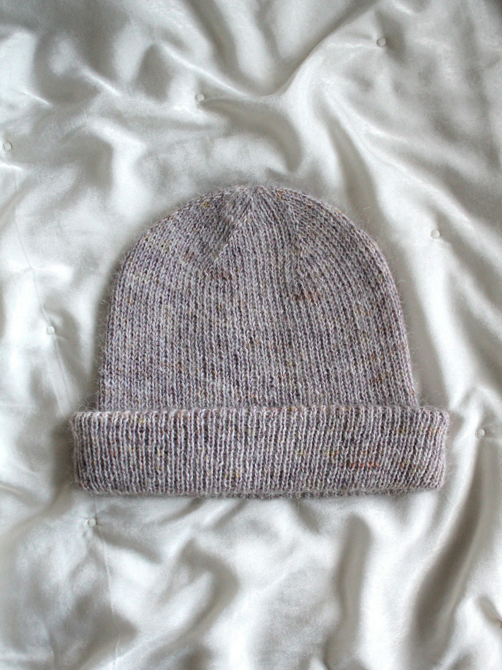 Un bonnet tricoté gris posé sur un drap