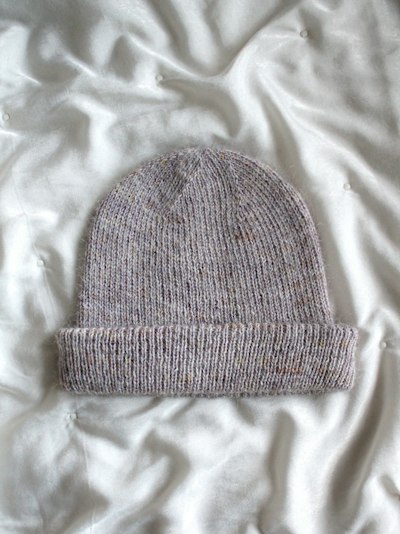 Un bonnet tricoté gris posé sur un drap