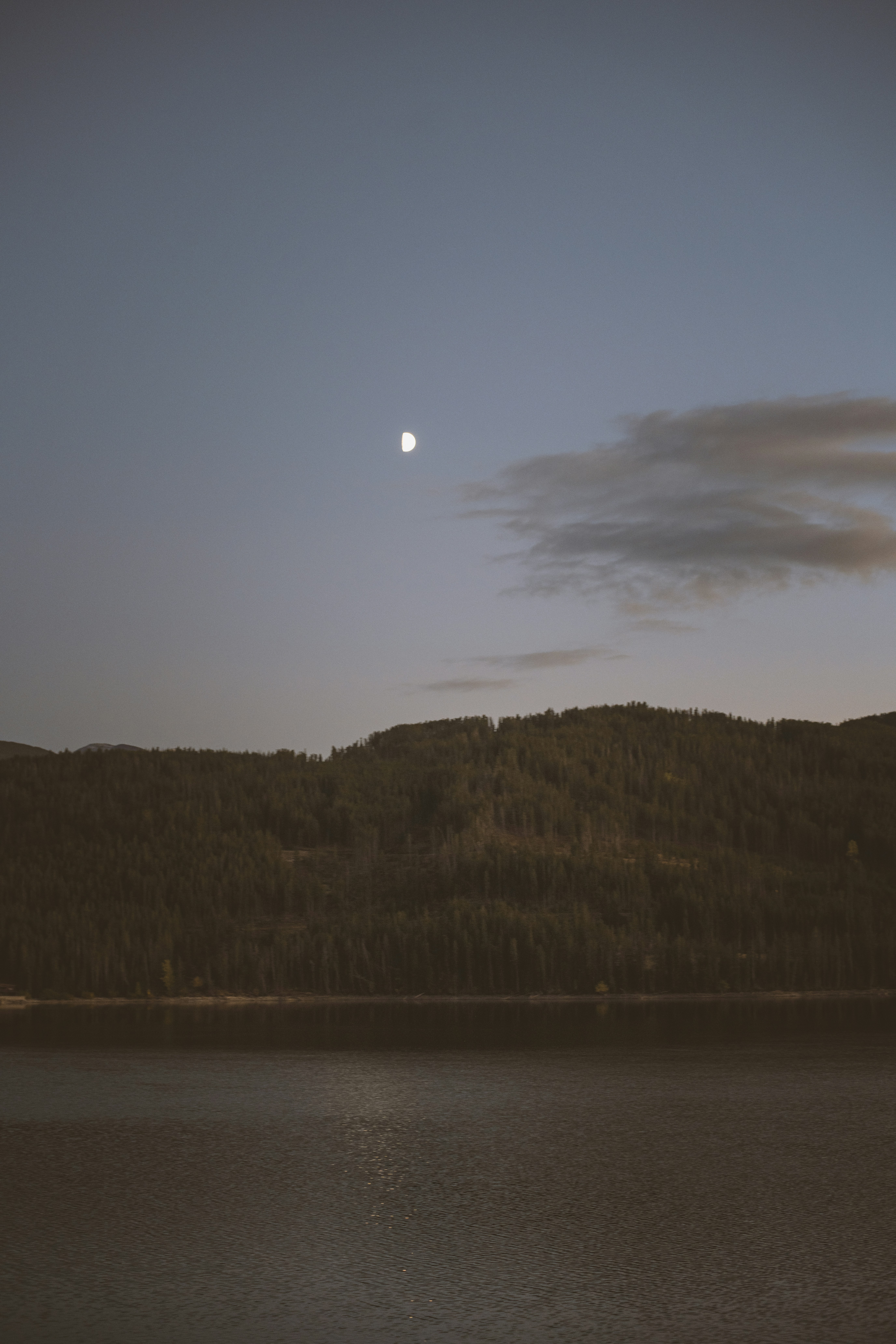 a body of water with a hill and a moon in the sky