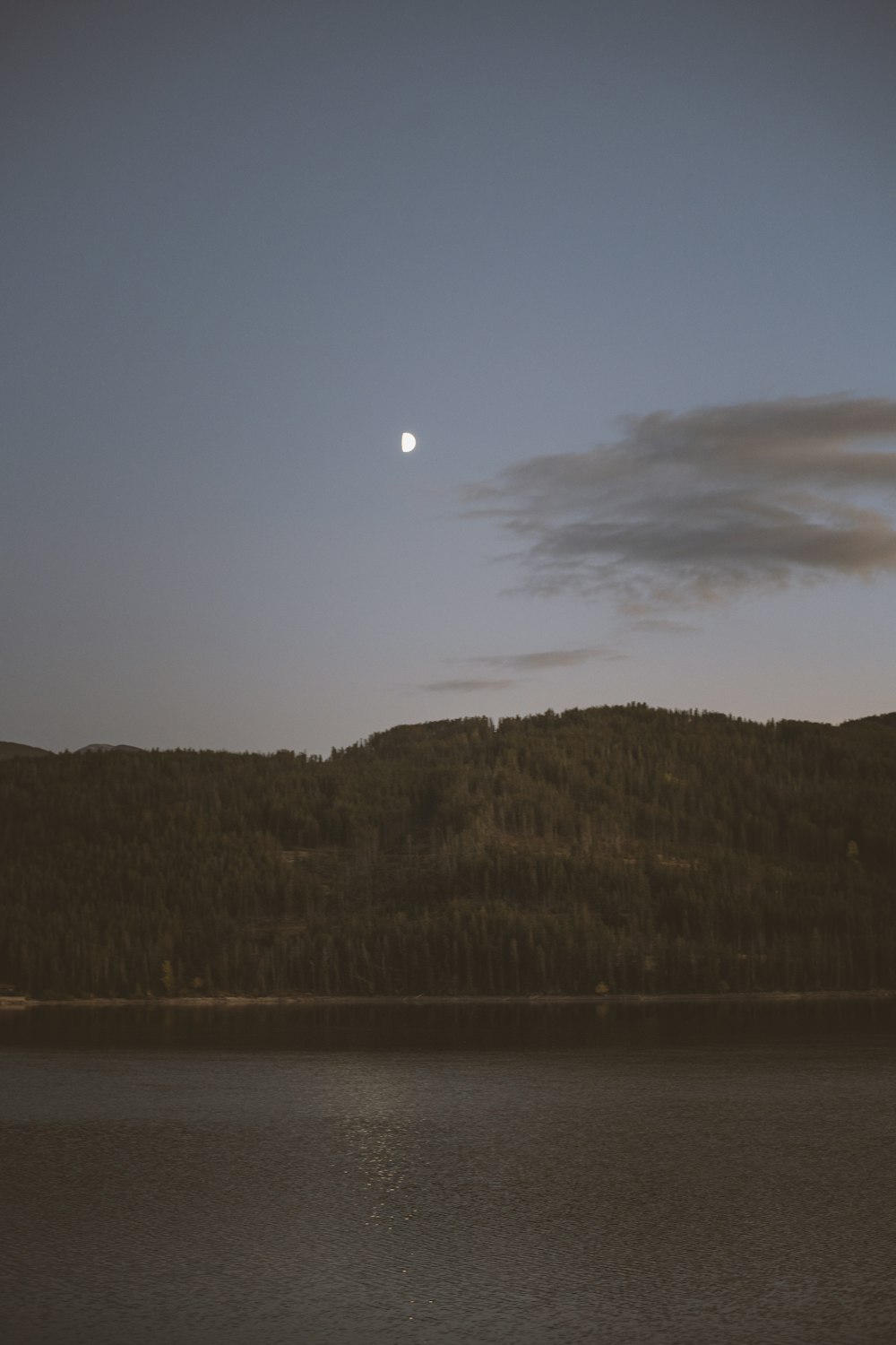 a body of water with a hill and a moon in the sky
