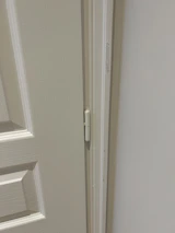 A handyman fixing a door hinge outdoors on a sunny day.