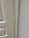 A close-up view of a door hinge on a light-colored door and frame. The door has a textured surface with panel detailing.