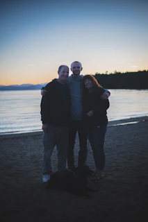 A smiling family holding their dog happily beside the Caldera coastline at sunset.