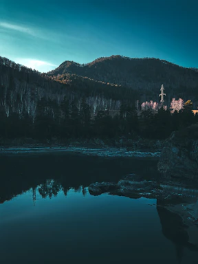 A rugged mountain landscape at dusk with deep forest greens and charcoal shadows, evoking a sense of calm and strength.