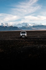 A rugged flatbed camper parked on a snowy Alaskan mountain trail at sunset.