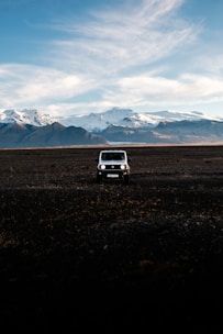 A rugged flatbed camper parked on a snowy Alaskan mountain trail at sunset.