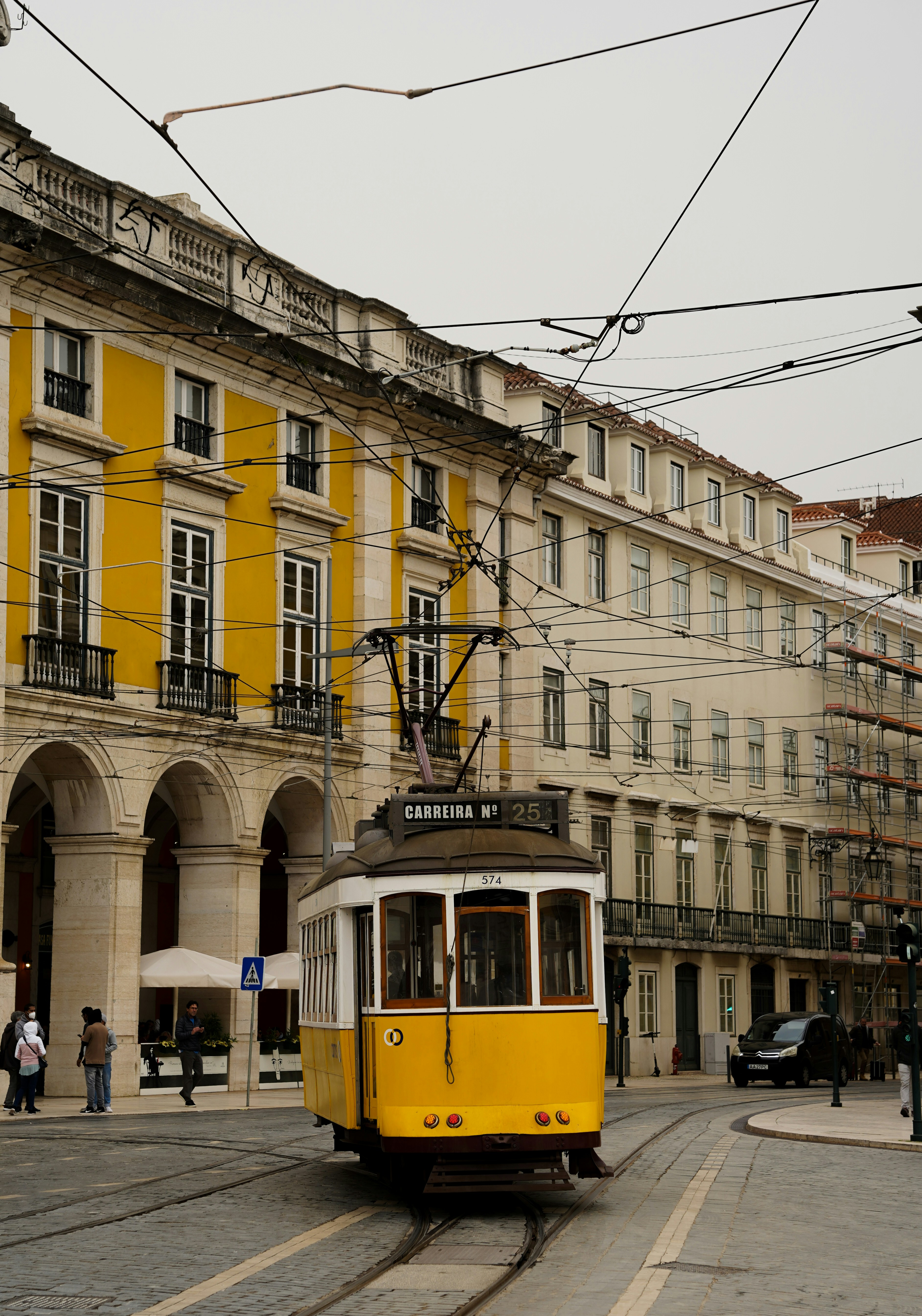 Tranvía amarillo subiendo calle empedrada de Lisboa con casas coloridas y azulejos, luz cálida de tarde