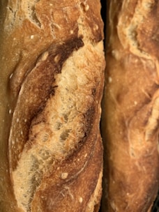 A close-up of golden, crusty baguettes stacked in a rustic bakery setting.