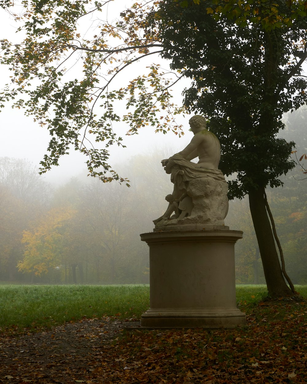 a statue of a person sitting on a stone pedestal in a park