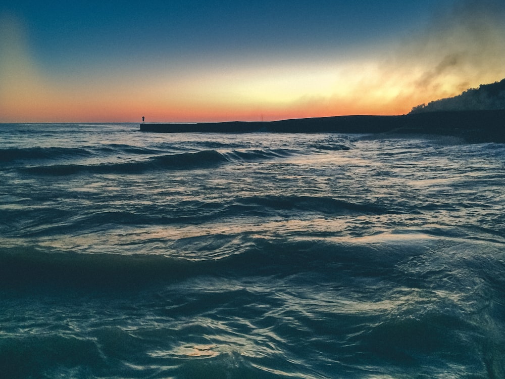 a body of water with waves and a sunset in the background