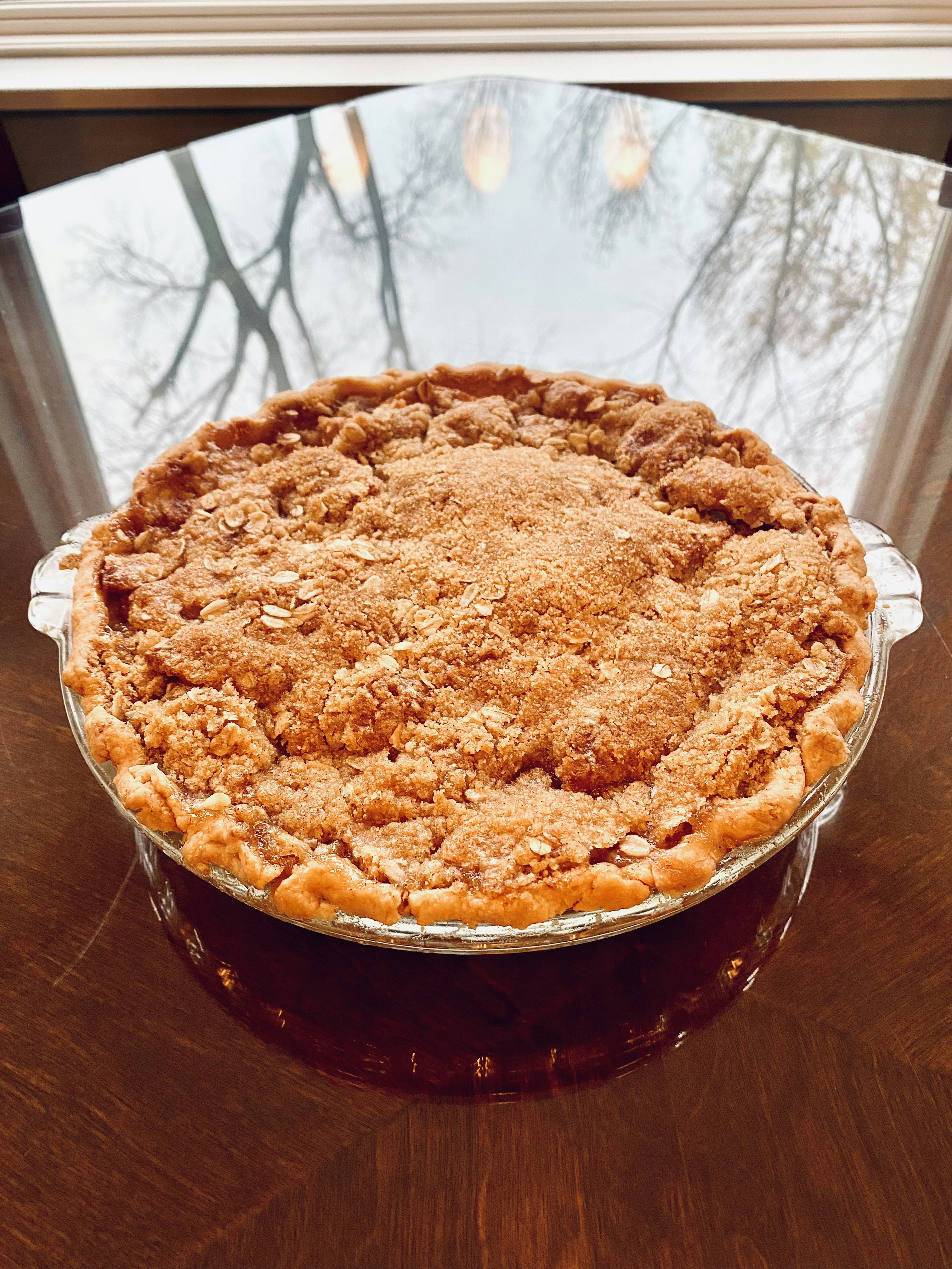 iPhone photo of Mom’s homemade apple pie on glass table for our thanksgiving day feast with trees and sky background in reflection