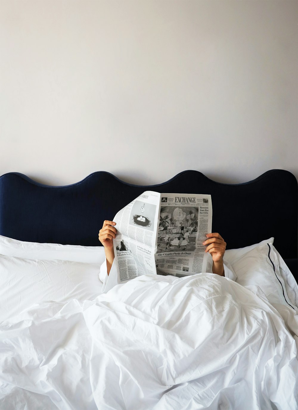 a person lying on a bed reading a newspaper