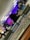 A digital audio mixing console with various colorful buttons and sliders is in the foreground, while a group of people is blurred in the background. The setting appears to be an indoor event with dynamic lighting.