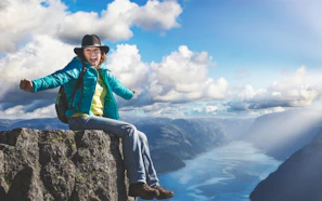 A joyful traveler standing on a cliff, arms wide open embracing the adventure.