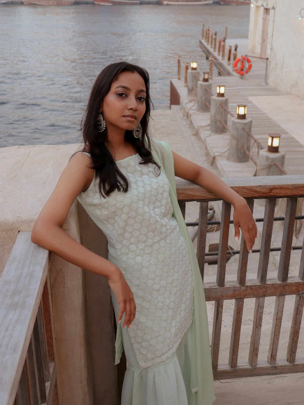 a woman in a dress standing on a bridge over water