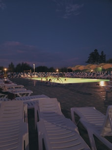 A beautifully lit pool at night with lounge chairs.