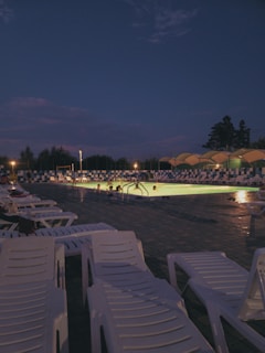A beautifully lit pool at night with lounge chairs.